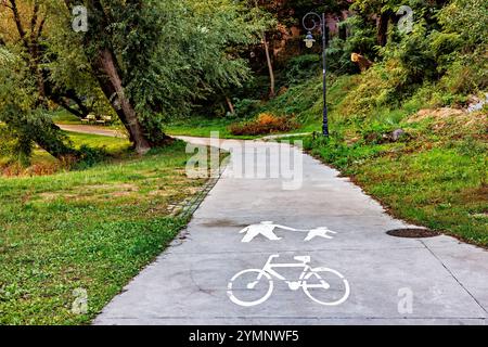 Ein Weg für Fußgänger und Radfahrer in einem Stadtpark, der mit einem entsprechenden Schild markiert ist. Grüne Bäume umher. Stockfoto