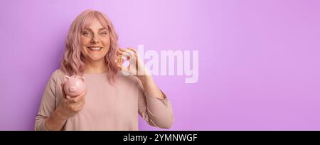 Junge kaukasische Frau, die Schweinebank und Bitcoin isoliert auf hellem Fliederhintergrund hält und einlädt, mit der Hand zu kommen. Stockfoto