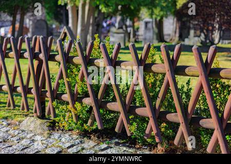 Schöner Holzzaun aus überkreuzten Pfählen vor dem Hintergrund eines grünen Rasens. Stockfoto