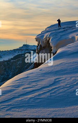 Ein Mann steht auf einem schneebedeckten Berghang bei Sonnenuntergang Stockfoto
