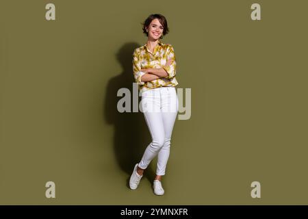 Selbstbewusste junge Frau mit brünetten Haaren in eleganter Bluse steht vor khakifarbenem Hintergrund und symbolisiert modernen Geschäftsstil und lässige Eleganz Stockfoto