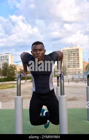 Junger schwarzer Mann, der Calisthenics-Dips in einem Fitnessstudio im Freien macht Stockfoto