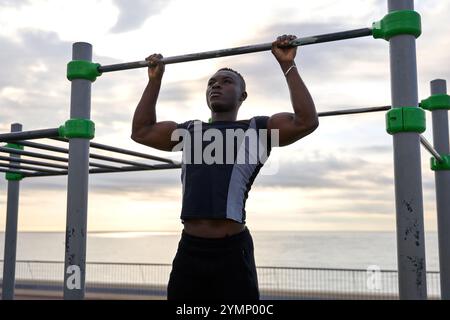 Junger schwarzer Mann, der bei Sonnenuntergang an der Pull-up-Bar am Strand Calisthenics vorführt Stockfoto
