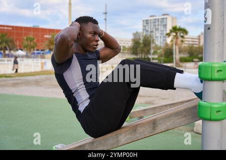 Schwarzer Mann, der Calisthenics-Sit-UPS in einem Fitnessstudio im Freien macht Stockfoto