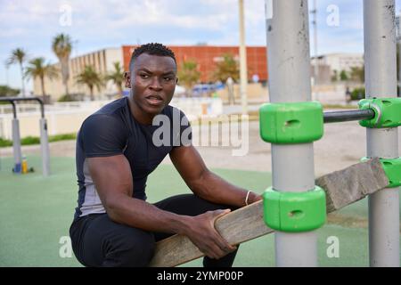 Junger schwarzer Mann, der Calisthenics-Übungen mit hölzernen parallettes-Bars im Fitnessstudio im Freien durchführt Stockfoto