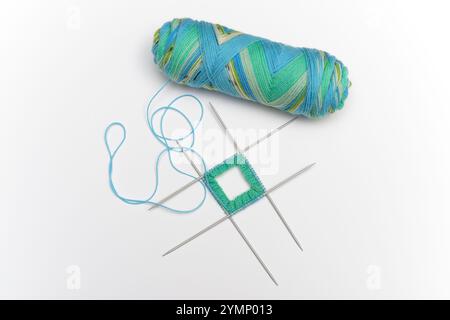 Ein Knäuel aus buntem, buntem Garn in Blau-, Grün- und Gelbtönen, zusammen mit einem kleinen Strickprojekt auf vier doppelzackigen Nadeln. Das Proje Stockfoto