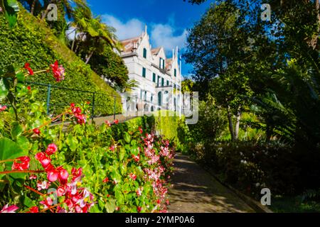 Ein ruhiges weißes Haus in malerischer Umgebung, erreichbar über einen Gartenweg, gesäumt von leuchtenden Blumen unter Sonnenlicht Stockfoto