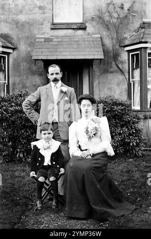 Ein Familienfoto nach einer Hochzeit. Der Mann steht mit einer Knopflochblume in der Jacke, die Dame sitzt mit einem raffinierten Blumenarrangement auf ihrer Bluse. Der Junge sitzt auch. Das Originalfoto stammt aus der Zeit um 1920 und wurde von der Redhill Photo Co der Station Road, Redhill, Surrey, England, aufgenommen. Stockfoto