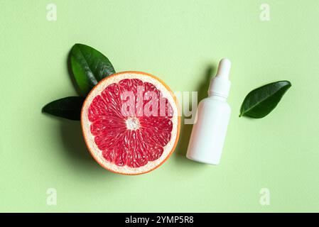 Leere Flasche ätherisches Grapefruitöl und frische Zitrusfrüchte mit grünen tropischen Blättern auf hellgrünem Hintergrund. Massageöl, Fruchtsäurepeeling, Vitam Stockfoto