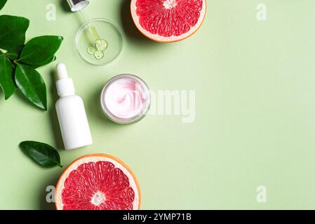 Leeres Etikett Serumflasche und Cremebecher auf grünem Hintergrund mit Petrischale und Grapefruit-Zitrusscheiben und grünen Blättern, Kopierraum. Schönheitscreme und Stockfoto