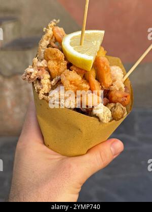 Eine Hand hält einen Kegel Fritto Misto, ein italienisches Streetfood. Diese spezielle Version enthält gebratene Calamari, Sardellen, Garnelen und Gemüse. Stockfoto