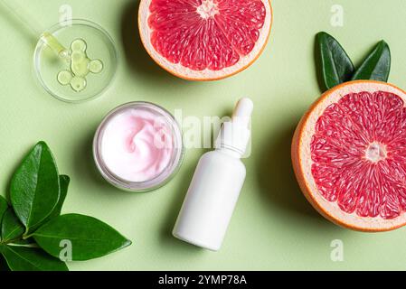 Leeres Etikett Serumflasche und Cremebecher auf grünem Hintergrund mit Petrischale und Grapefruit-Zitrusscheiben und grünen Blättern. Schönheitscreme und Serum mit Stockfoto