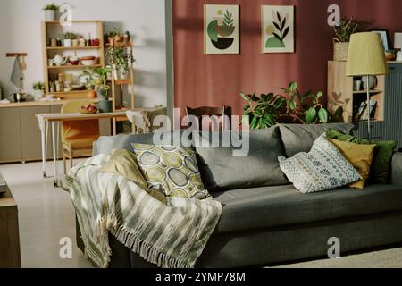 Gemütliches Wohnzimmer mit einem komfortablen Sofa mit gemusterten Kissen, umgeben von grünen Pflanzen und Holzmöbeln, die die warme Atmosphäre unterstreichen Stockfoto