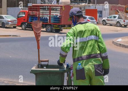 Straßenreiniger, Rückblick auf arabische Herkunft Mann in Uniform sammelt Straßenmüll in Müllcontainer während extremer Hitzewelle Stockfoto