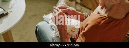 Ältere Frau in orangefarbenem Kleid, die Hände mit jemandem hält. Das Bild zeigt einen intimen Moment, der von der Seite aufgenommen wurde und Details zu ihrer Kleidung und Umgebung zeigt Stockfoto
