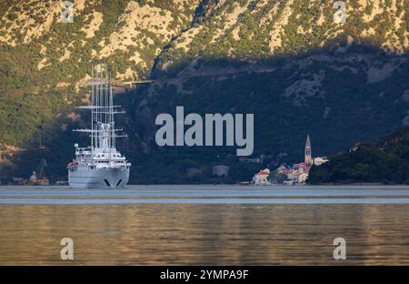 Ein großes Segelschiff gleitet am frühen Morgen durch die ruhigen Gewässer der Kotor Bay und passiert die historische Stadt Perast, Montenegro. Sonnenlicht weich Stockfoto