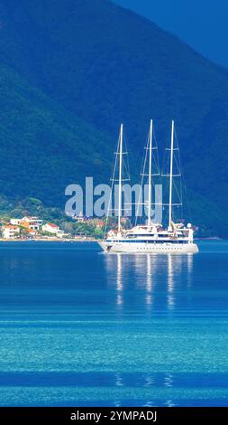 Eine ruhige Szene in der Bucht von Kotor, Montenegro, kurz vor dem Regen. Ein weißes Segelboot schwimmt auf ruhigem, türkisfarbenem Wasser, umgeben von üppig grünen Bergen Stockfoto