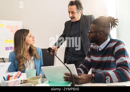 Leitender Business Mentor, der sich bei einem zwanglosen Büro-Meeting informell mit jungen Fachleuten aus unterschiedlichen Bereichen unterhalten und dabei die generationenübergreifende Arbeit demonstriert Stockfoto