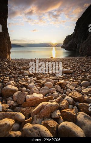 Versteckte Bucht und Strand mit einem alten Bergdorf. Der Sonnenaufgang spiegelt sich im Wasser. Eine wunderschöne Landschaft, eingerahmt von Klippen und der Adria Stockfoto