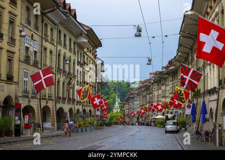 Wunderschöne alte Hauptstraße mit altem Gebäude und Flaggen an einem regnerischen Tag in Bern, Kanton Bern, Schweiz. Stockfoto