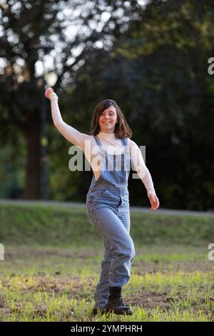 Sorglose junge Frau, die einen sonnigen Tag im Park genießt, tanzt und Freude ausdrückt Stockfoto