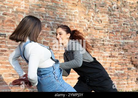 Zwei fröhliche junge Frauen kitzeln sich gegenseitig und haben Spaß an einer Ziegelmauer Stockfoto