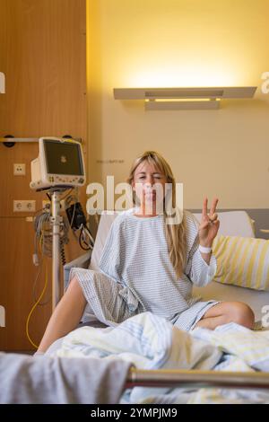 Eine Patientin in einem modernen Krankenhausraum nach komplexer Operation an einem Schulterbruch. Freuen Sie Sich. Zeigt ihre Zunge, lächelt, macht ein Zeichen von victor Stockfoto