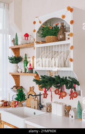 Wunderschön angeordnete Küchenregale, die mit Fichtengirlanden, Weihnachtsbaum und Ornamenten dekoriert sind. Innenraum der Küche, weiße Ablagen dekoriert Stockfoto