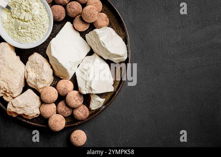 Essbare Karamell Ton Steine, Ton Felsen und Pulver auf schwarzem Hintergrund, Draufsicht, Kopierraum. Natürliche essbare Kalziumkreide und Tonkugeln zum Essen. Stockfoto