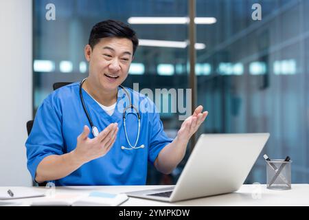 Asiatischer Mann Arzt führt virtuelle Beratung mit Laptop. Stethoskop und blaue Peelings zeigen, dass medizinisches Fachpersonal sich mit der Online-Patientenkommunikation befasst. Stockfoto