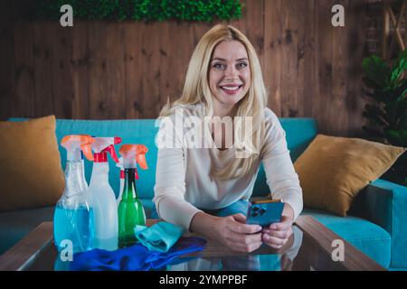 Foto von positiver guter Laune Frau gekleidetes weißes Hemd, das Hausarbeit macht und modernes Gadget im Wohnraum kommuniziert Stockfoto