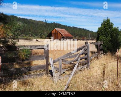 Eine rote Scheune befindet sich auf einer Wiese, umgeben von einem kaputten Holzzaun in einem abgelegenen Bergtal in Nordkalifornien. Stockfoto