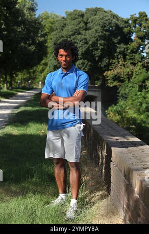 Porträt eines selbstbewussten jungen Athleten, der mit überkreuzten Armen in einem Park steht und eine entspannte und sportliche Einstellung zeigt Stockfoto