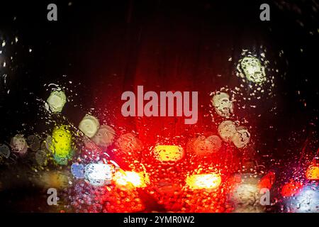Reflektionen roter Bremslichter von einer Autoscheibe im Regen im Stau. Sicherheit im Straßenverkehr. Schlechte Sicht Stockfoto