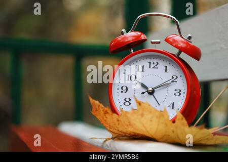 Herbstzeit. Wecker und gefallenes Blatt auf Holzbank im Freien, Platz für Text Stockfoto
