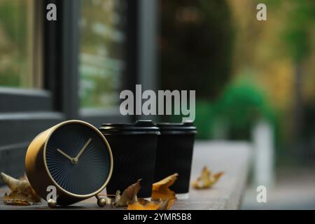 Herbstzeit. Wecker, gefallene Blätter und Tassen mit heißen Getränken in der Nähe des Cafés im Freien, Platz für Text Stockfoto