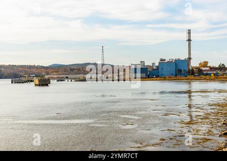 Erdgaskraftwerk am Ufer eines Flusses. Bewaldete Hügel auf dem Gipfel der Herbstfarben stehen im Hintergrund. Stockfoto