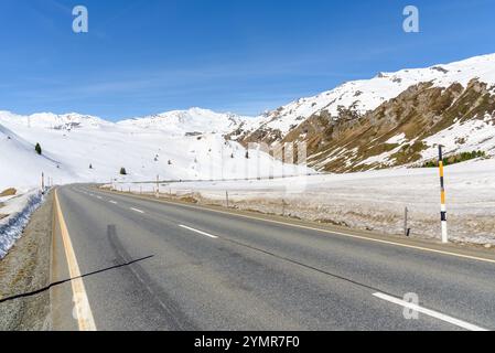 Leere Straße einer Passstraße zwischen verschneiten Hängen in den Schweizer Alpen an einem sonnigen Tag Stockfoto