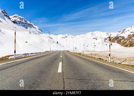 Leere geradlinige Passstraße durch schneebedeckte Gipfel in den Schweizer Alpen an einem sonnigen Tag Stockfoto