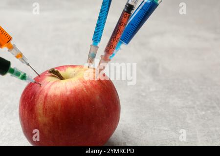 GVO-Konzept. Roter Apfel mit Spritzen auf grauem, strukturiertem Tisch, Nahaufnahme Stockfoto