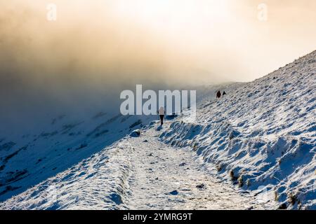 Silhouette von Wanderern auf einem schneebedeckten Berg mit niedriger Wolke und Sonne am späten Nachmittag Stockfoto