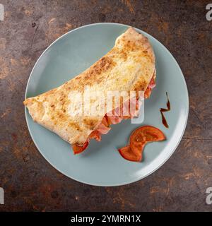 Geschlossene Pizza oder Calzone, gefüllt mit Lachs, Tomaten und Mozzarella, serviert auf einem Teller mit frischem Basilikum und Tomatenscheiben Stockfoto