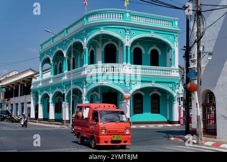 Ein rotes Tuk-Tuk passiert ein grünes Gebäude im chinesisch-portugiesischen Stil. Mit typischen Bogenfenstern; an der Ecke Dibuk Rd./Yaowarat Rd. Phuket Town, Thailand Stockfoto