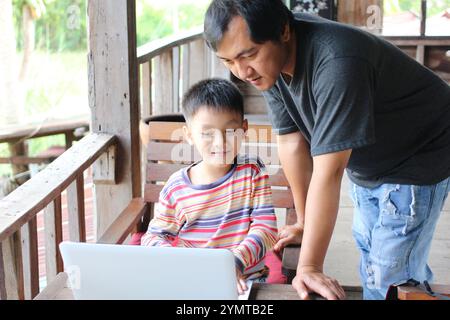 Ein Vater und ein Sohn teilen einen freudigen Moment, während sie gemeinsam ein Notebook erkunden. Ihre Verbindung unterstreicht den Wert von Familienzeit und Lernen. Stockfoto