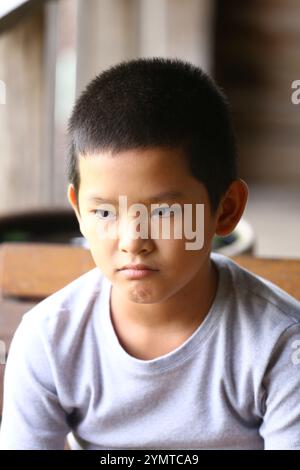 Ein nachdenklicher kleiner Junge mit ernstem Ausdruck sitzt ruhig drinnen und zeigt eine Reihe von Emotionen und Unschuld in einer natürlichen Umgebung. Stockfoto