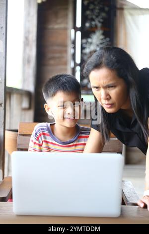 Eine Mutter und ihr Sohn teilen einen freudigen Moment, während sie mit einem Laptop interagieren. Dieses Bild fängt die Wärme des familiären Interesses in einer zwanglosen Umgebung ein, emp Stockfoto