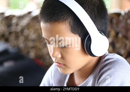 Ein kleiner Junge genießt Musik mit Kopfhörern und zeigt einen Moment der Konzentration und Entspannung. Das Bild fängt die Freude des Audioerlebnisses in einem cas ein Stockfoto