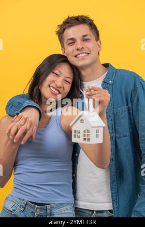 Glückliches Paar, das Hausmodell auf hellgelbem Hintergrund hält. Vertikal Stockfoto