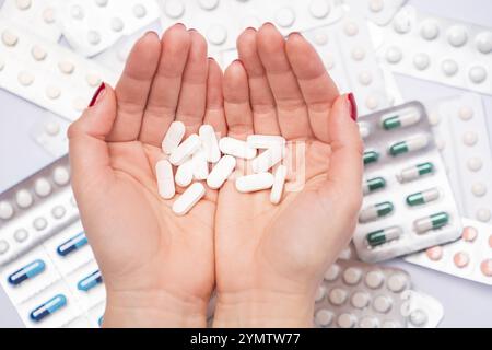 Weibliche Hand mit vielen pharmazeutischen Pillen und Kapseln, farbenfrohe Medikamententabletten in Blisterpackungen im Hintergrund. Stockfoto