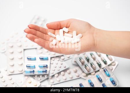 Weibliche Hand mit vielen pharmazeutischen Pillen und Kapseln, farbenfrohe Medikamententabletten in Blisterpackungen im Hintergrund. Stockfoto